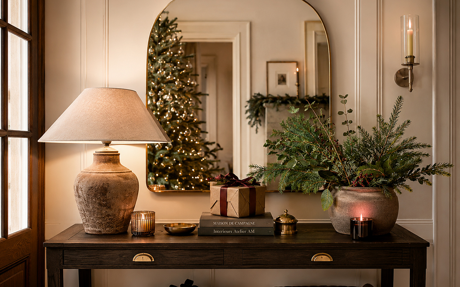 Console de Noël avec grand miroir arrondi, lampe en céramique, vase et petit cadeau.