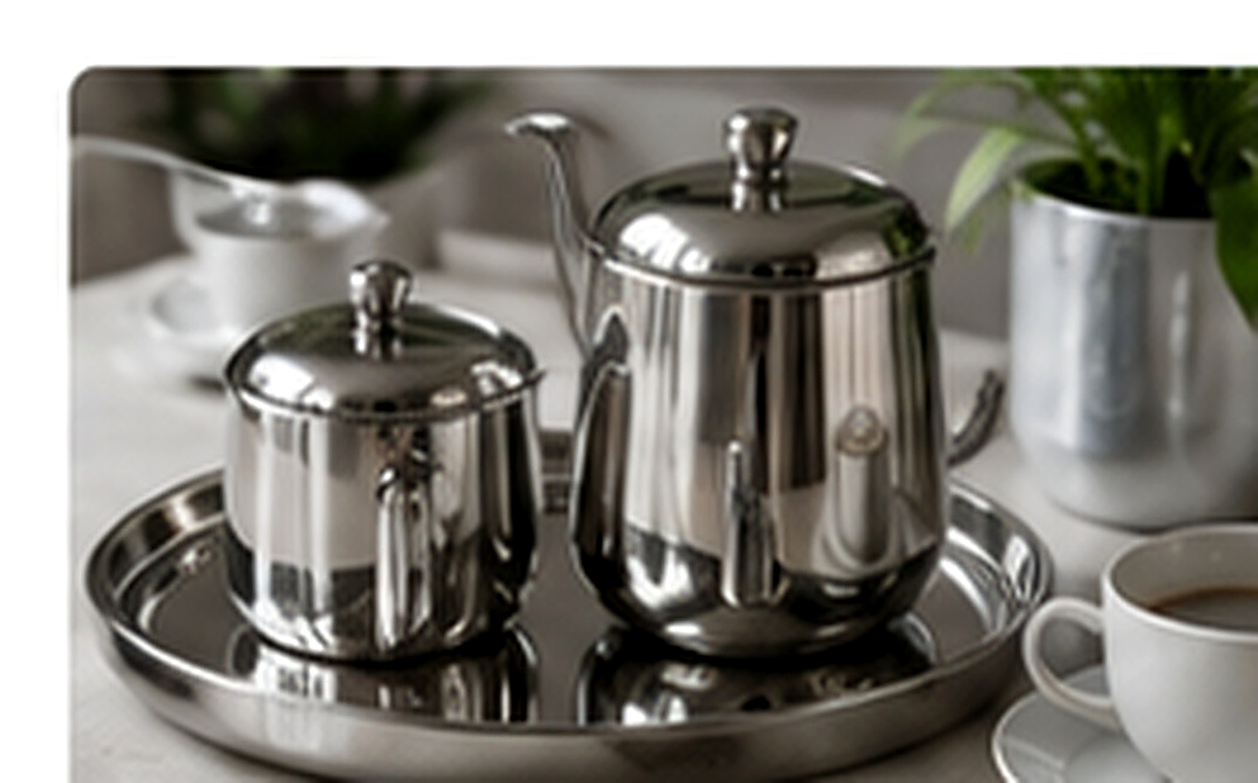 Théière et cafetière en acier inoxydable poli posées sur un plateau métallique.