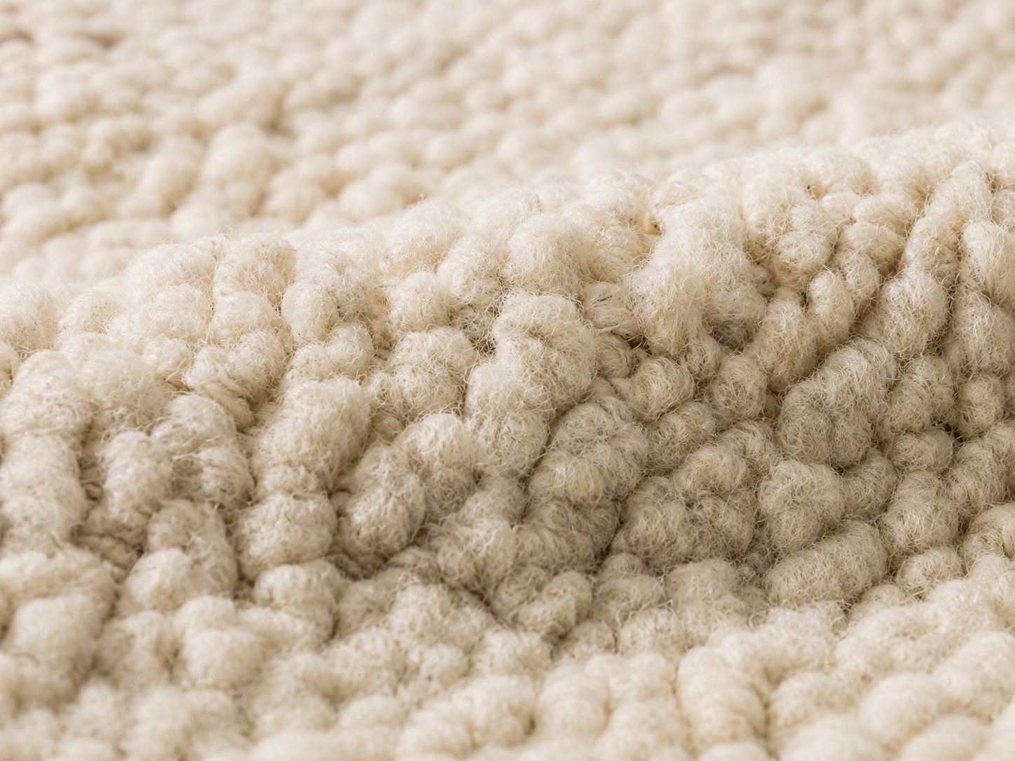 Gros plan sur les fibres épaisses d’un tapis en laine écrue à entretenir avec précaution.