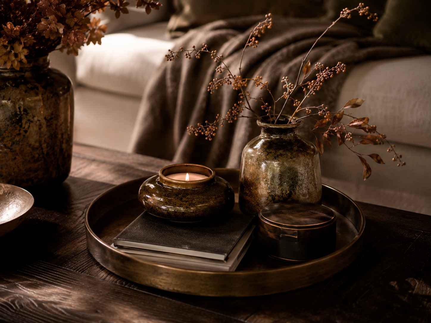 Petit geste déco automnal avec coussin vert mousse, photophore ambré, livres et vase en céramique.