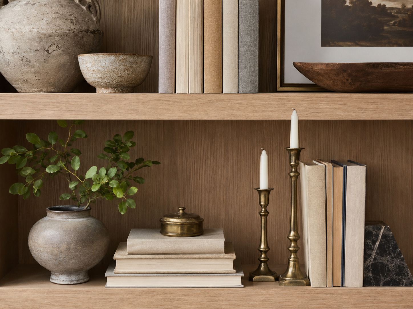 Composition décorative avec vase, livres empilés et bougeoirs de hauteurs différentes