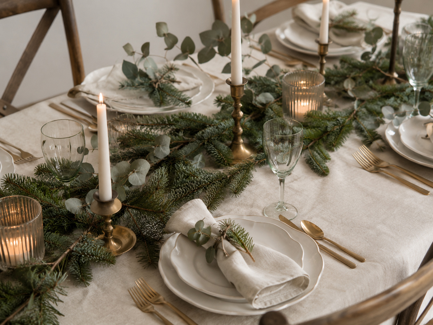 Table de Noël naturelle avec branches de sapin, laiton, lin clair et bougies blanches.