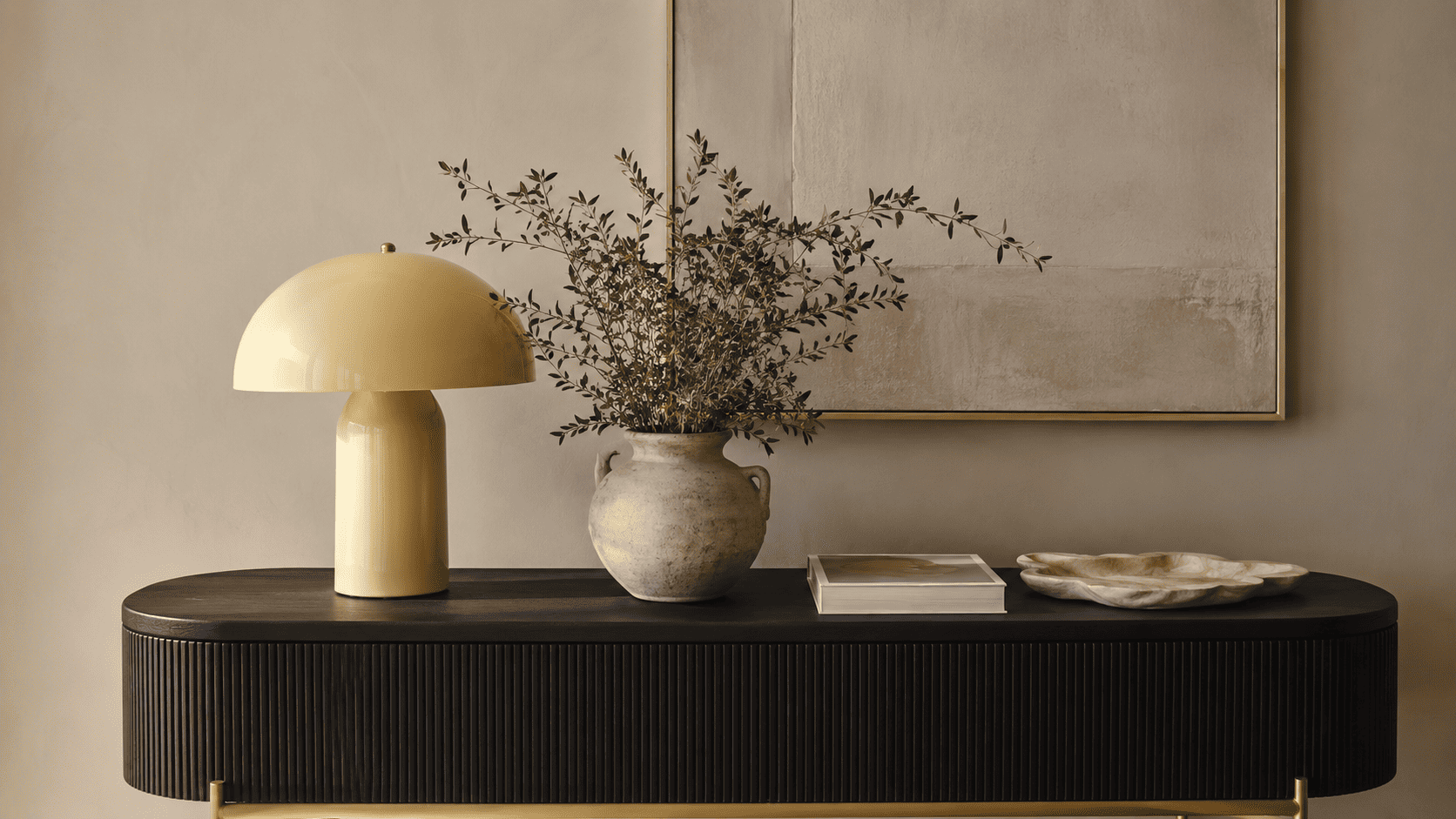 Lampe jaune beurre, vase céramique, livre d’art et objets déco sur une console contemporaine.