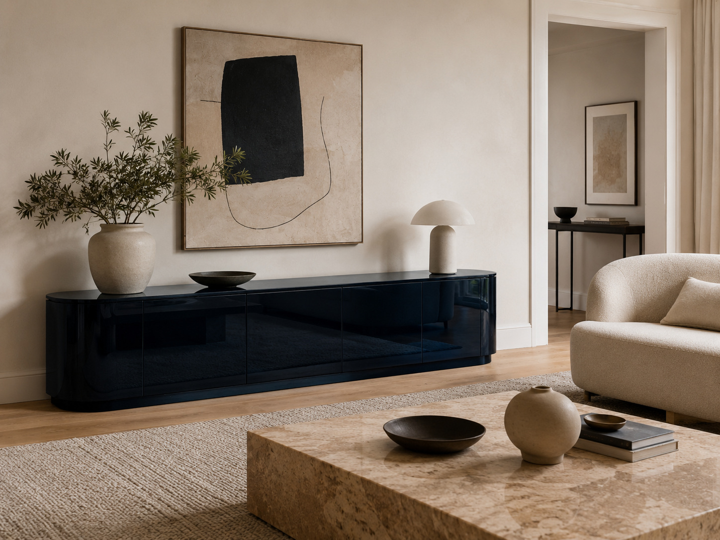 Salon épuré avec meuble noir laqué bas, fond clair, fauteuil crème et table basse en pierre.