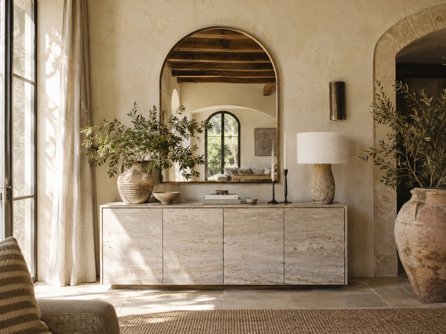 Buffet bas minéral et grand miroir en arche dans un intérieur méditerranéen baigné de soleil.