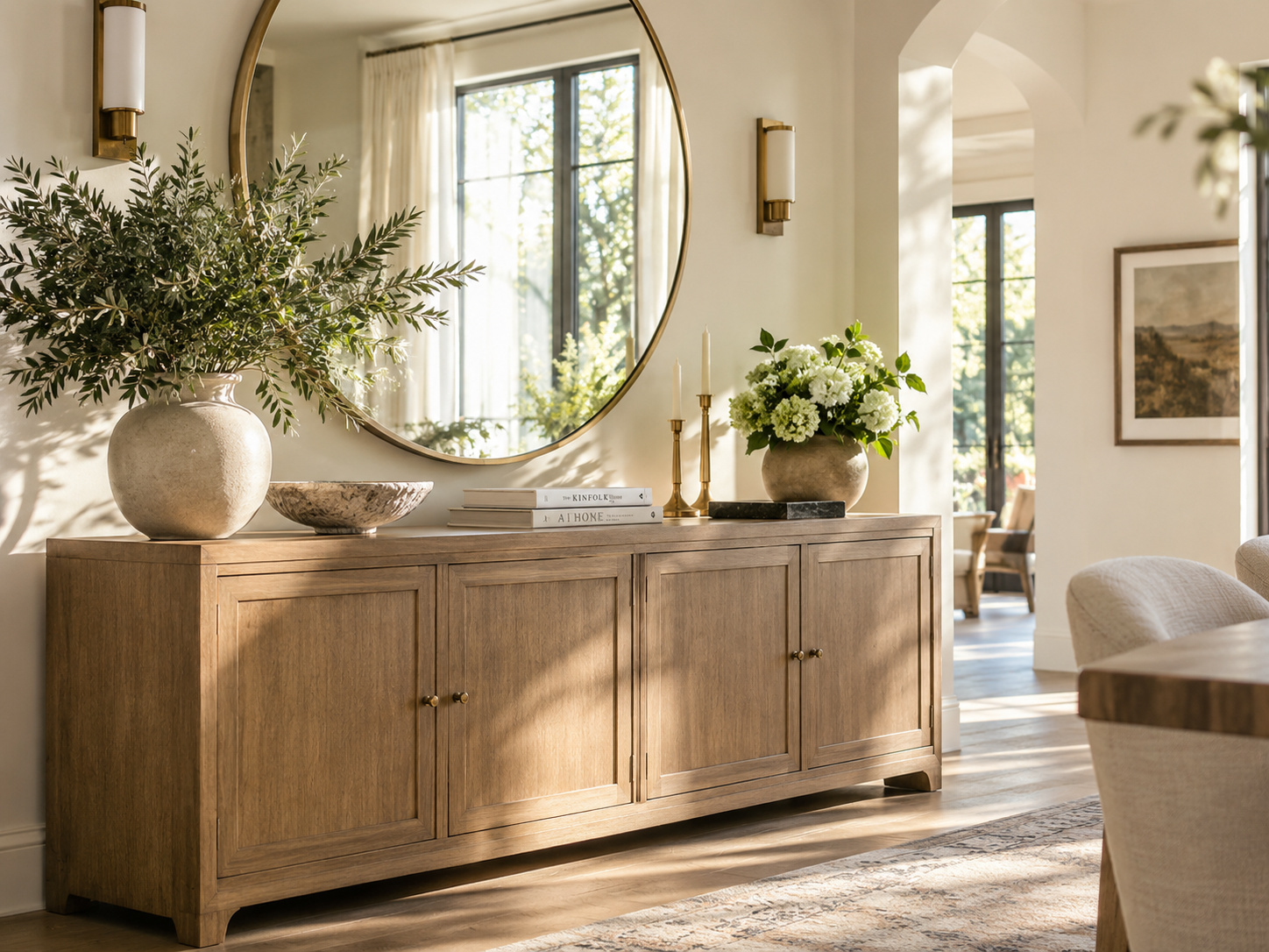 Buffet en bois clair et grand miroir rond dans un intérieur lumineux aux proportions équilibrées.