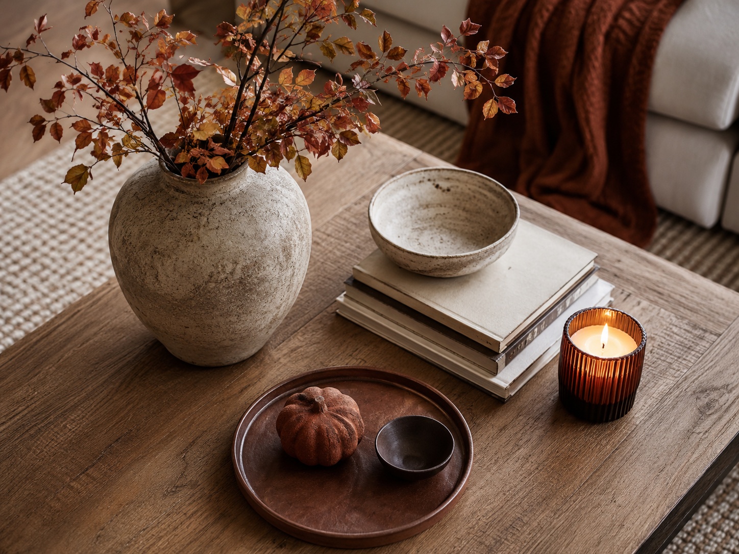 Objets déco d’automne réunis sur une table : céramiques, bougie, vase et petit végétal.
