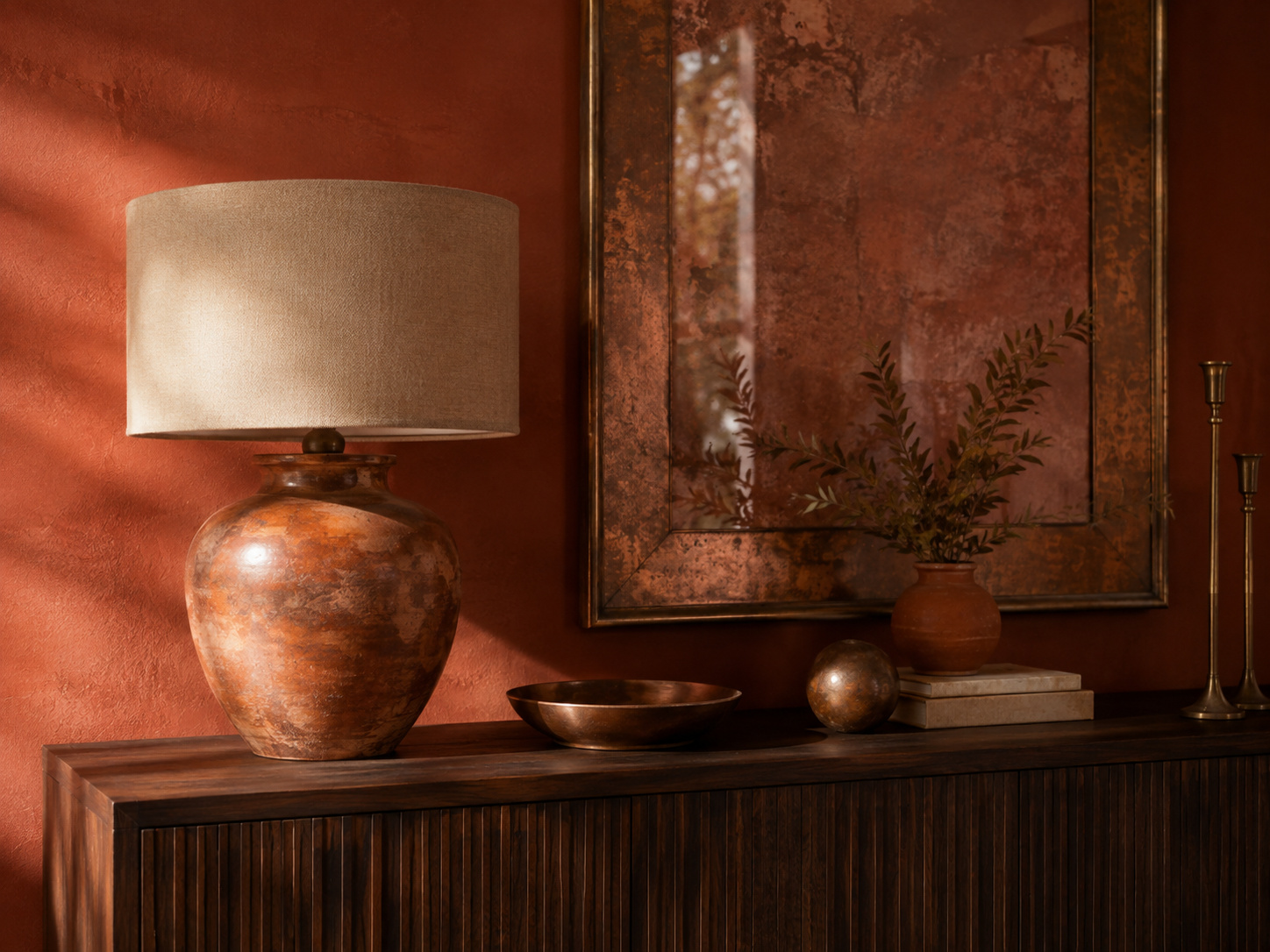 Console terracotta avec lampe en céramique, bois foncé, miroir patiné et bougeoirs en laiton.