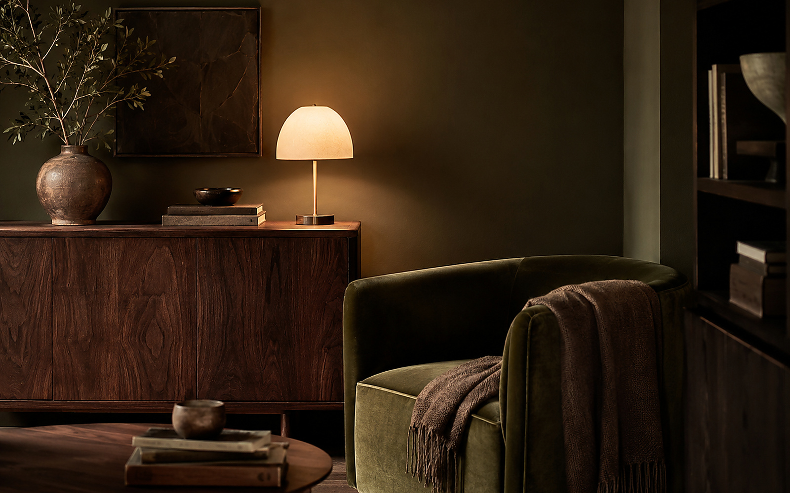 Coin lecture enveloppant avec fauteuil vert olive, meuble en noyer foncé et lumière chaude.